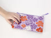 Purple pouch with floral designs and 'More Aloha' text held by a hand on a white background