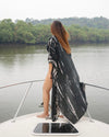 Woman in a black and white patterned dress standing on a boat with a river and trees in the background