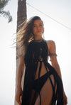 Woman wearing a black fringe dress standing next to a palm tree.