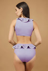 Woman wearing a purple bikini with ruffled details on a beige background