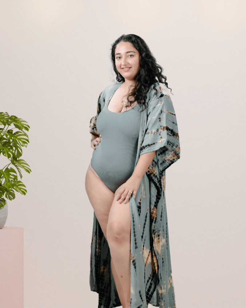 Woman wearing a gray swimsuit with a patterned cover-up against a plain background