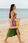 Woman holding a tote bag with beach-themed design on a sandy beach.
