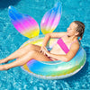 Person lounging on a colorful inflatable mermaid tail pool float in clear blue water.