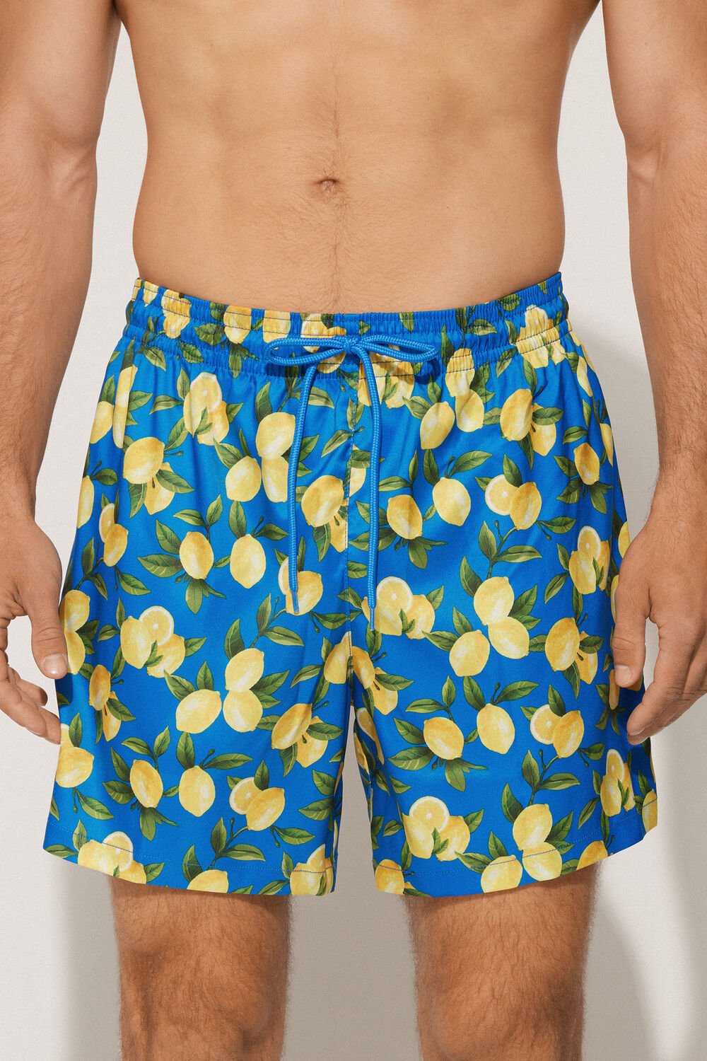 Blue swim shorts with lemon pattern worn by a person on a plain background