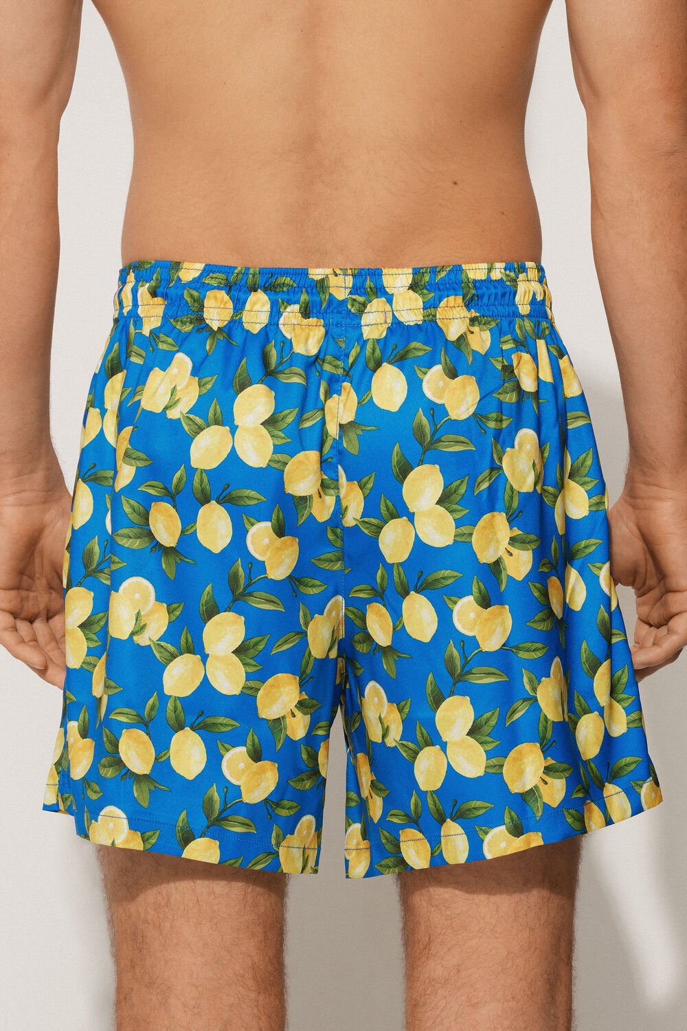 Blue swim shorts with lemon pattern worn by a person on a plain background